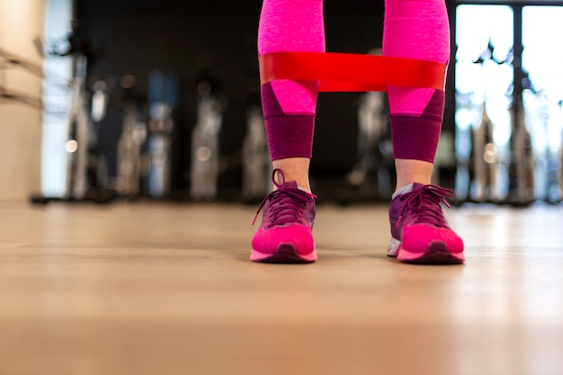 Mujer joven en ropa deportiva ejercicio deportivo con banda de goma en forma en las piernas en el gimnasio. Fitness y estilo de vida saludable