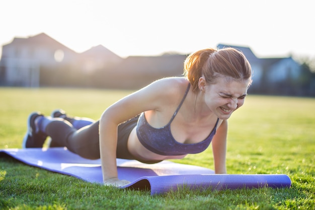 Mujer joven en ropa deportiva entrenamiento en campo al amanecer.