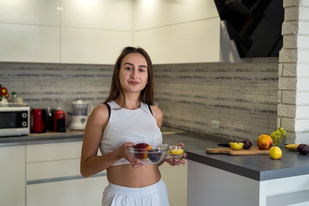 Mujer joven en ropa deportiva con frutas en casa. Estilo de vida saludable