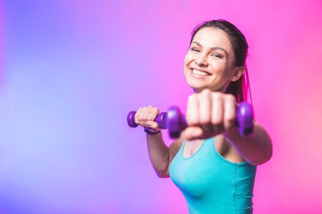 Mujer joven en ropa deportiva con hermosa sonrisa sosteniendo mancuernas de peso haciendo ejercicio físico