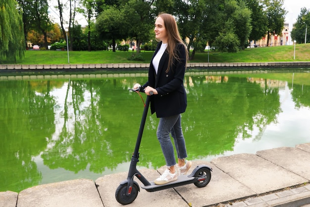 Una mujer joven con ropa elegante posa con un scooter eléctrico en la calle