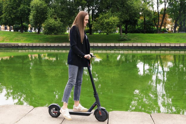 Una mujer joven con ropa elegante posa con un scooter eléctrico en la calle