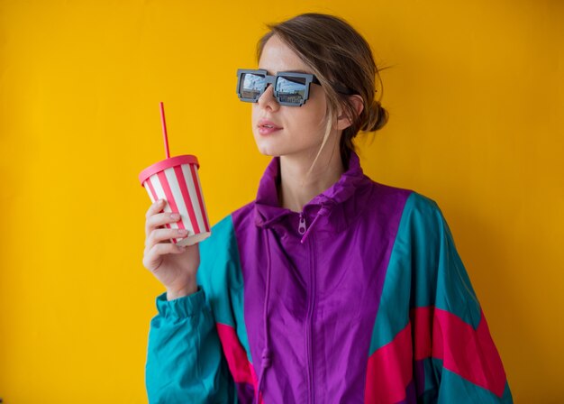 Mujer joven en ropa de estilo años 90 con taza en amarillo