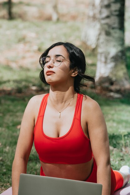 Mujer joven en ropa de fitness haciendo un ejercicio de yoga mientras cierra los ojos relajándose en el parque