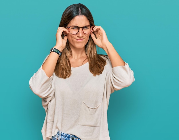 Mujer joven con ropa informal y gafas que cubren las orejas con los dedos con expresión molesta por el ruido de la música a todo volumen concepto sordo