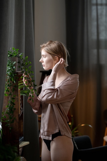 Mujer joven en ropa interior elegante cuidando sus plantas ella de pie en la habitación