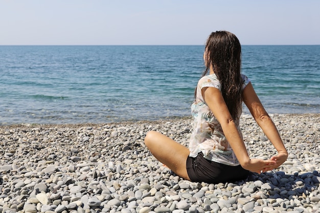 Mujer joven con ropa mojada se sienta en la playa de guijarros y estira las manos detrás de la espalda