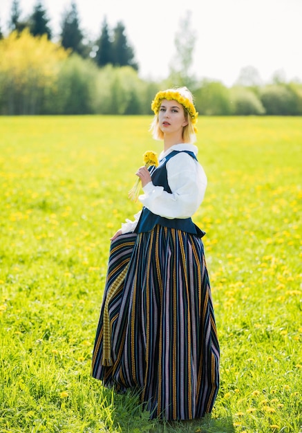 Mujer joven en ropa nacional con corona de diente de león amarillo en el campo de primavera ligo