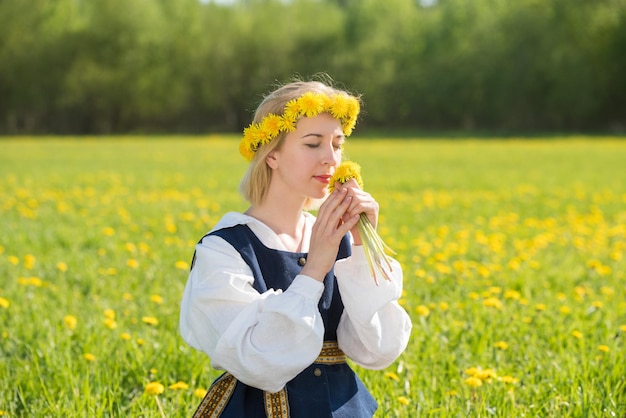 Mujer joven en ropa nacional con corona de diente de león amarillo en el campo de primavera primavera