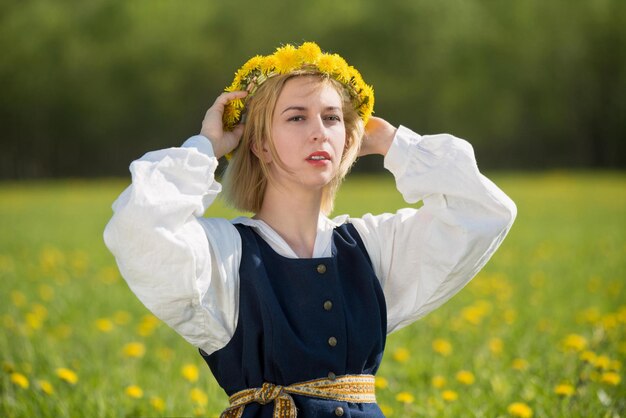 Mujer joven en ropa nacional con corona de diente de león amarillo en el campo de primavera