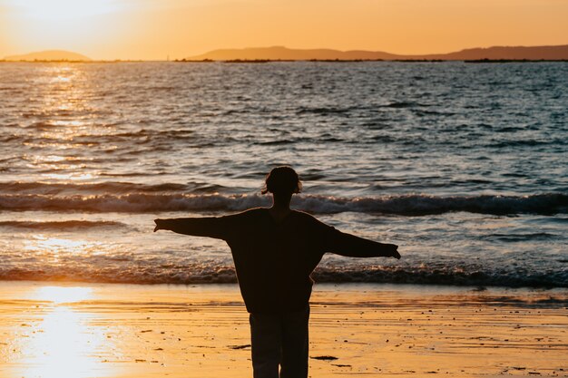 Mujer joven en ropa de primavera en la playa durante una puesta de sol