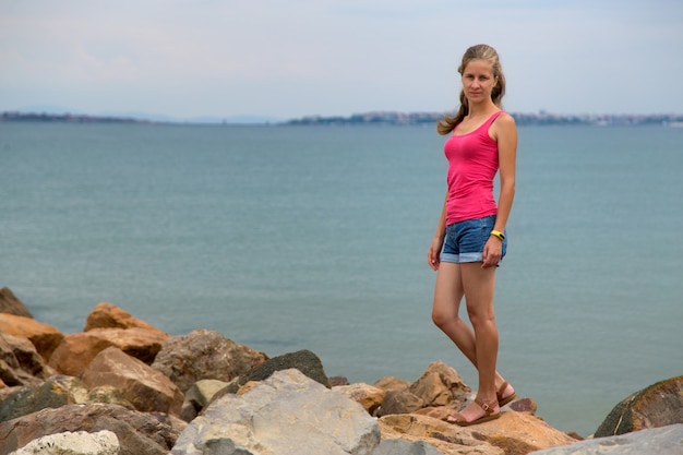 Mujer joven en ropa de verano de pie en la orilla del mar.