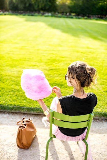 Mujer joven con rosa algodón de azúcar sentado al aire libre en el parque
