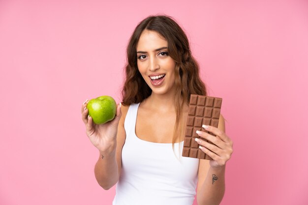 Mujer joven rosa tomando una tableta de chocolate en una mano y una manzana en la otra