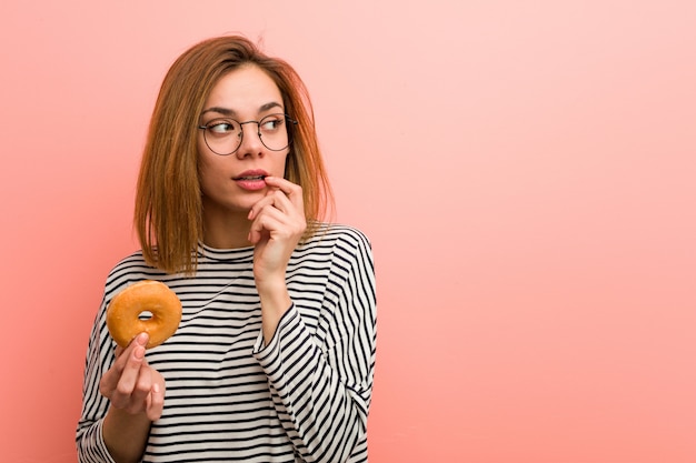 Mujer joven con una rosquilla relajada pensando en algo mirando a.