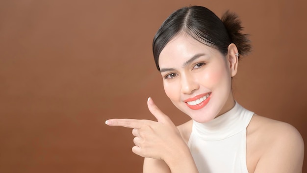 Una mujer joven con un rostro hermoso sonriendo tocándose la cara sobre marrón