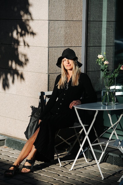 Mujer joven rubia cubierta con sombrero de ala ancha y vestido negro de manga larga