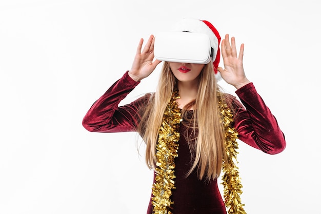 Foto mujer joven rubia con un gorro de papá noel y un casco de realidad virtual