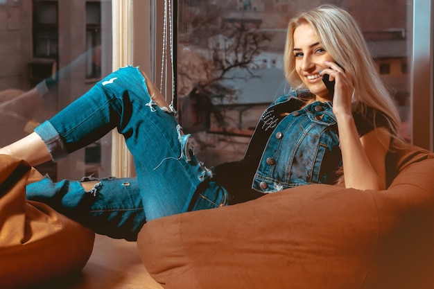 Mujer joven rubia hablando por teléfono y sonriendo en ropa casual. Concepto de relax, refrigerio y ocio