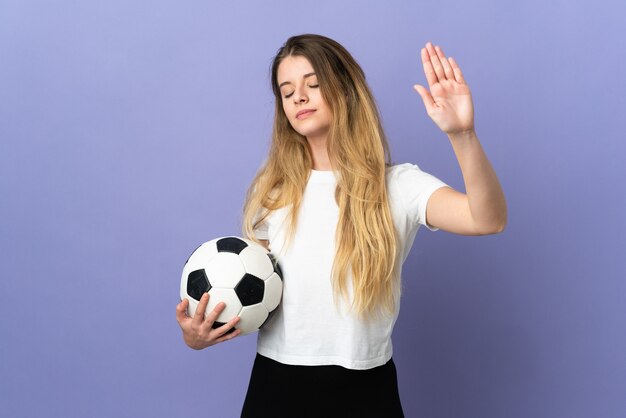 Mujer joven rubia jugador de fútbol aislada sobre fondo púrpura haciendo gesto de parada y decepcionado