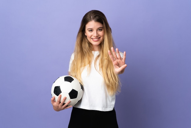 Mujer joven rubia jugador de fútbol posando aislada contra la pared en blanco