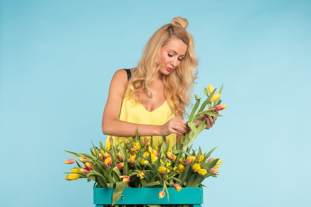 Mujer joven rubia con ramo de tulipanes sobre fondo azul.