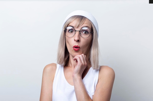 Mujer joven rubia sorprendida en gafas sombrero blanco sobre un fondo claro