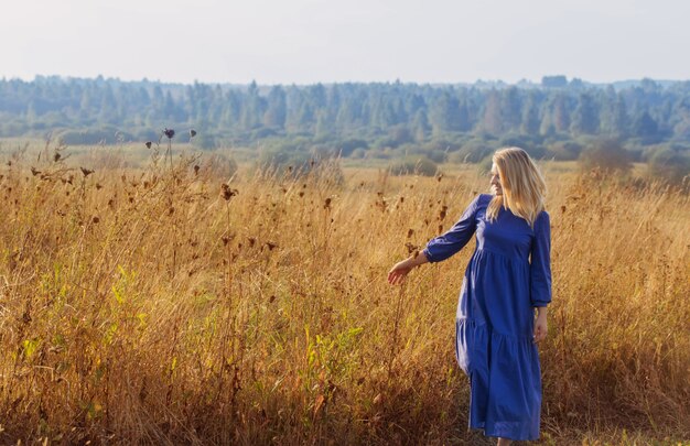 Mujer joven rubia en vestido azul en el campo al atardecer