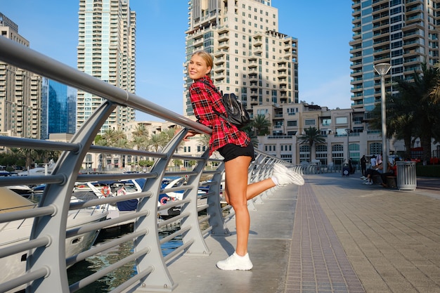 Mujer joven rubia viajes caminando por la calle al aire libre en la ciudad de Dubai. Marina de Dubai en Emiratos Árabes Unidos.