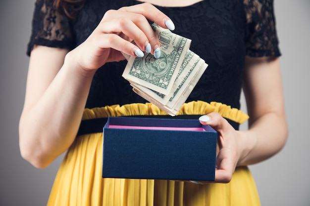 Mujer joven saca dinero de una caja de regalo