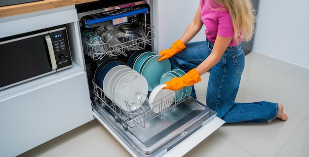 Una mujer joven saca los platos de la lavadora de platos