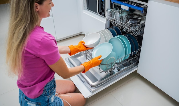 Una mujer joven saca los platos de la lavadora de platos