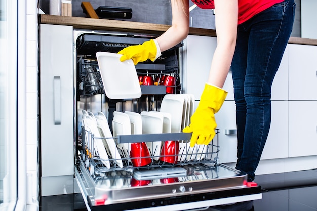 Mujer joven sacando platos limpios de la máquina lavavajillas.