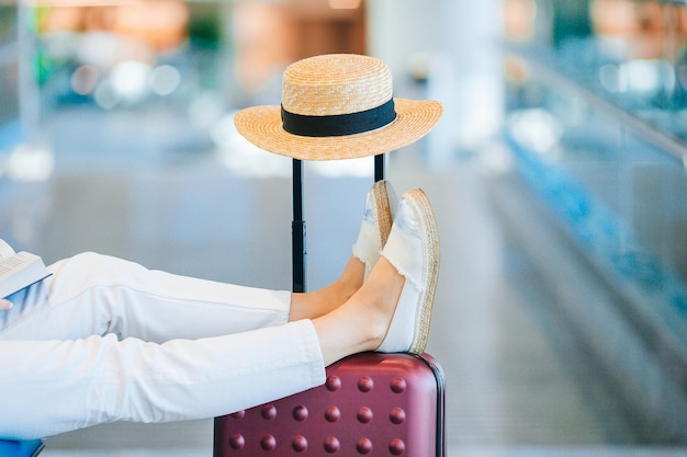 Mujer joven en un salón del aeropuerto esperando aterrizar con las piernas cerradas en el equipaje