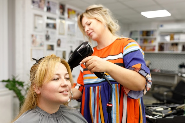Mujer joven en un salón de peluquería Peluquería seca el cabello de los clientes Centrarse en el cliente