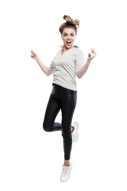 Una mujer joven salta alegremente Una hermosa mujer rubia con una camiseta negra, jeans y zapatillas blancas Actividad energética y positiva Aislada sobre fondo blanco Altura completa vertical