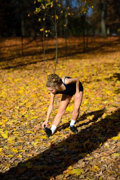 Mujer joven sana calentando estirando sus brazos en el camino al aire libre, sesión de jogging en el parque.