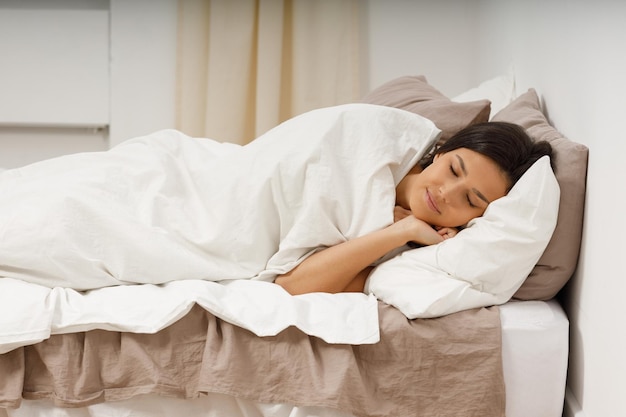 Mujer joven sana cubre manta durmiendo con los ojos cerrados en la cama en el dormitorio
