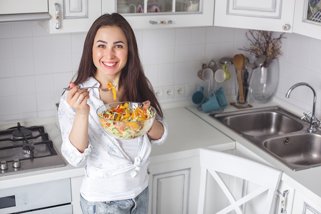 Mujer joven sana que come la ensalada en la cocina