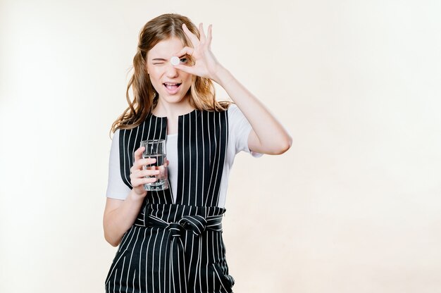 Mujer joven sana sonriente que sostiene una píldora de vaso de agua