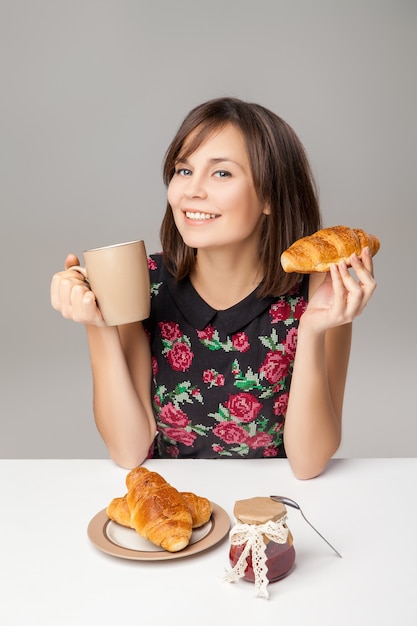 Mujer joven sana con taza y croissants de desayuno