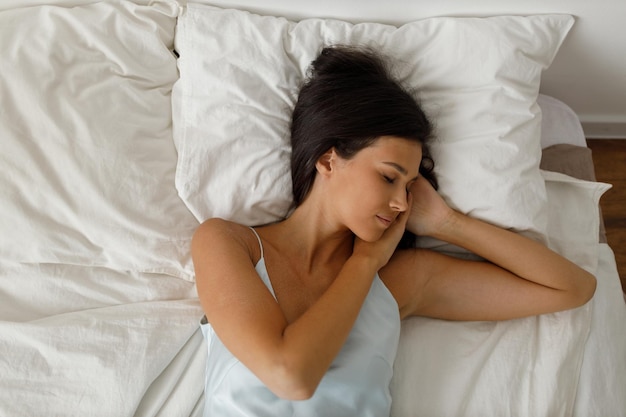 Mujer joven sana vistiendo camisón acostado en la cama en el dormitorio