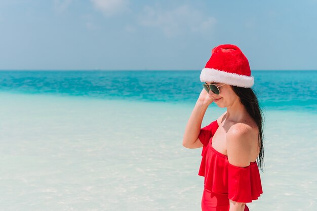 Mujer joven en Santa Hat caminando extendió sus manos en la playa de arena blanca