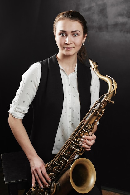Mujer joven con saxofón sobre fondo negro