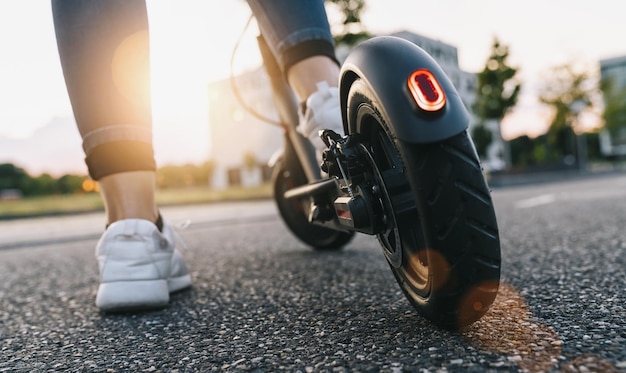 Mujer joven en el scooter eléctrico en la carretera al atardecer