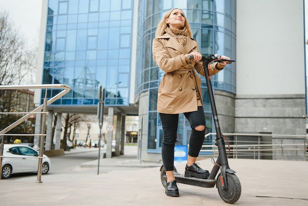 Mujer joven con scooter eléctrico en la ciudad