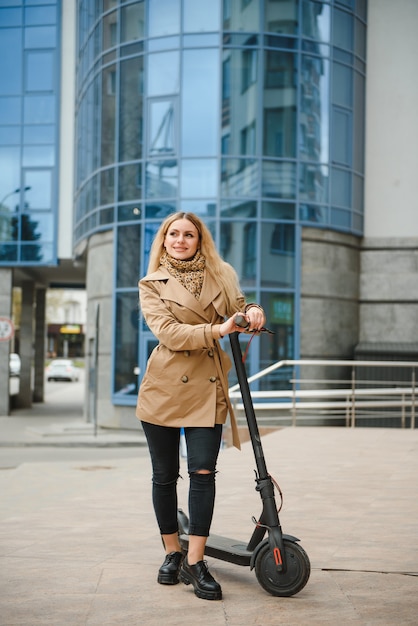 Mujer joven con scooter eléctrico en la ciudad