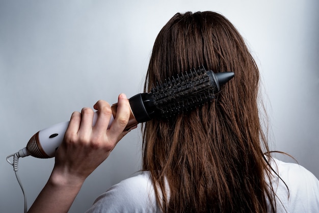 Mujer joven con secador de pelo y peine cepillándose el pelo.