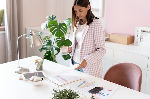 Mujer joven segura en ropa casual elegante sonriendo mientras está de pie cerca de su lugar de trabajo