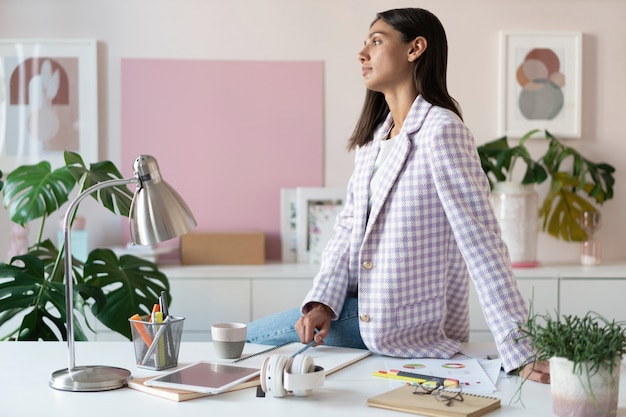 Foto mujer joven segura en ropa casual elegante sonriendo mientras está de pie cerca de su lugar de trabajo